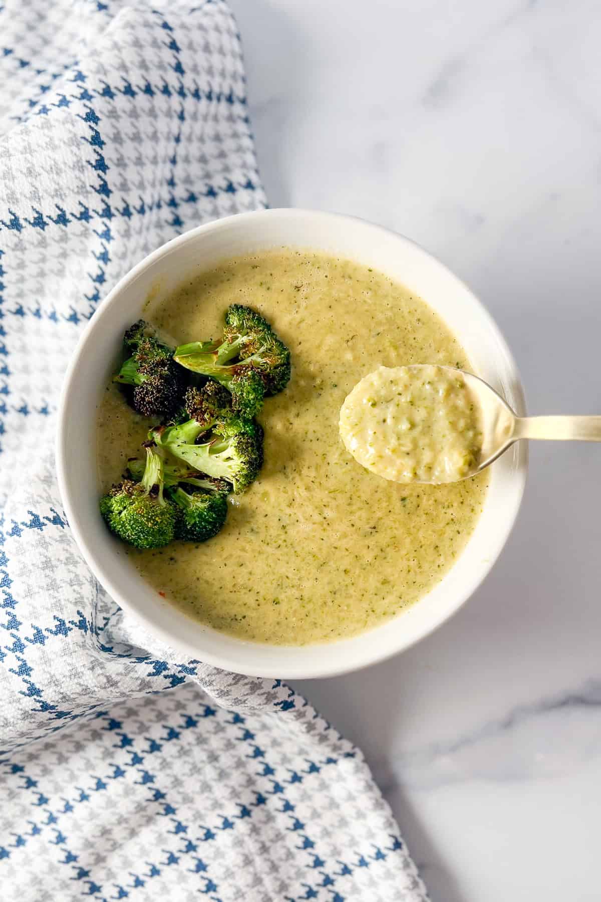 A bowl of vegan cream of broccoli soup with roasted broccoli on top and a spoon.