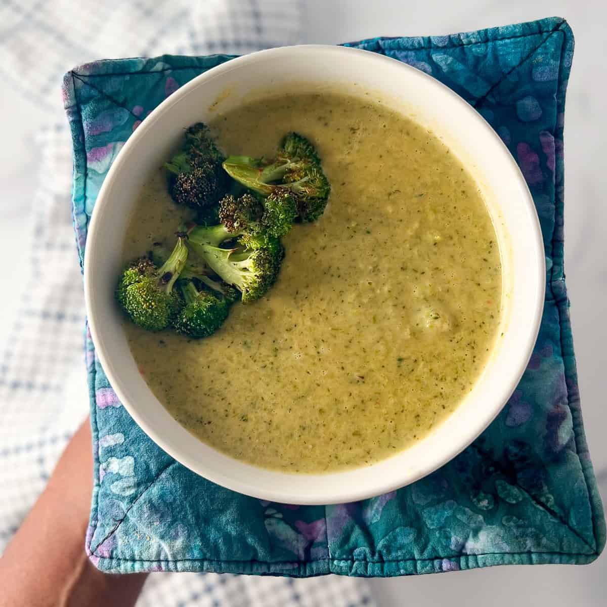 A woman's hand holding a bowl of vegan cream of broccoli soup.