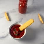 A bowl of ketchup with a fry being dipped in.