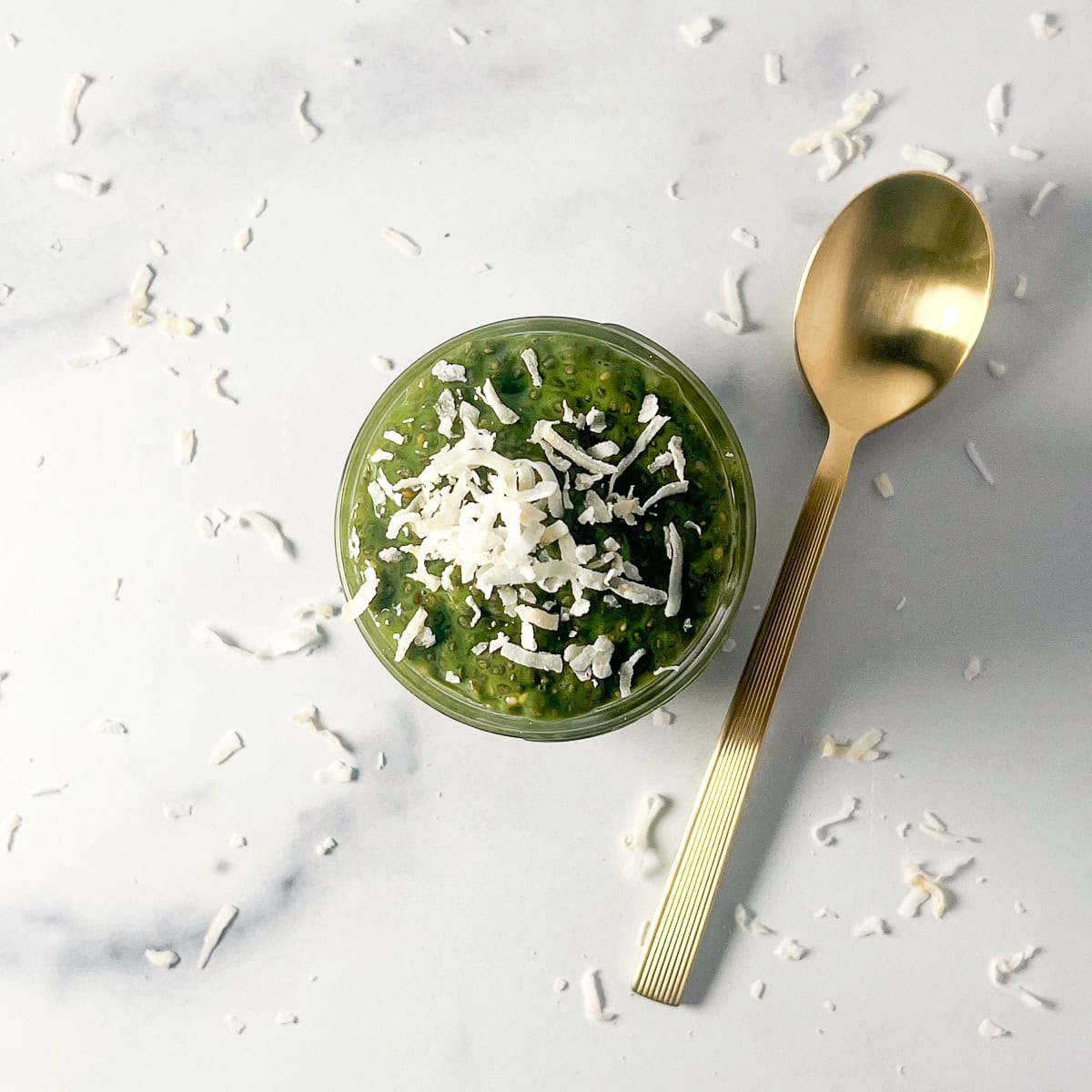 Matcha chia pudding in a small jar topped with shredded coconut and a spoon on the side.