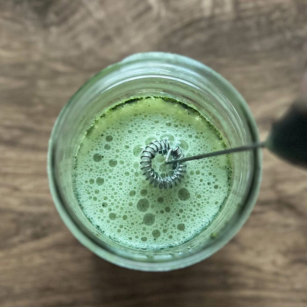Matcha and soy milk being combined with a hand frother.