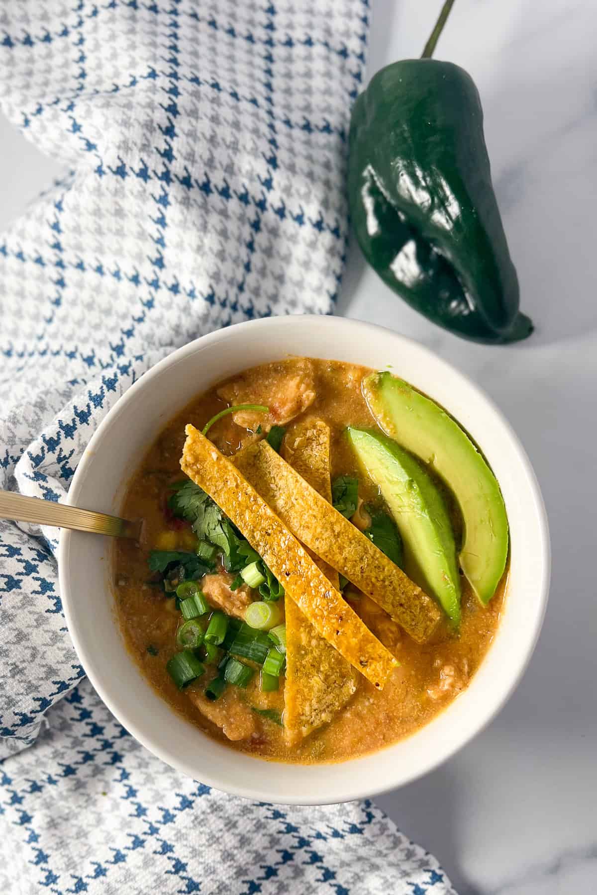Vegan chicken tortilla soup in a bowl topped with sliced avocado, and poblano pepper on the side.