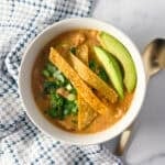 A bowl of vegan chicken tortilla soup topped with sliced avocado and a spoon on the side.
