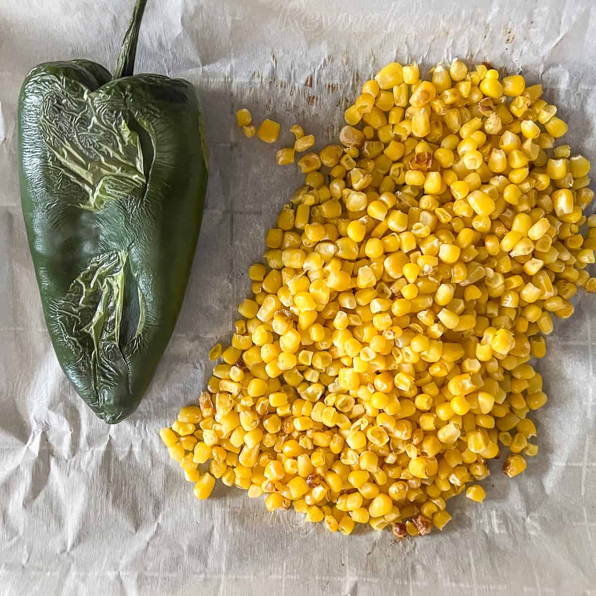 Roasted poblano pepper and corn on a parchment lined baking sheet.