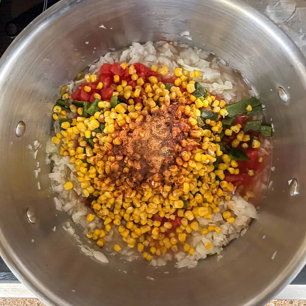 Onions, corn, bell pepper, and other veggies and seasonings in the pot.