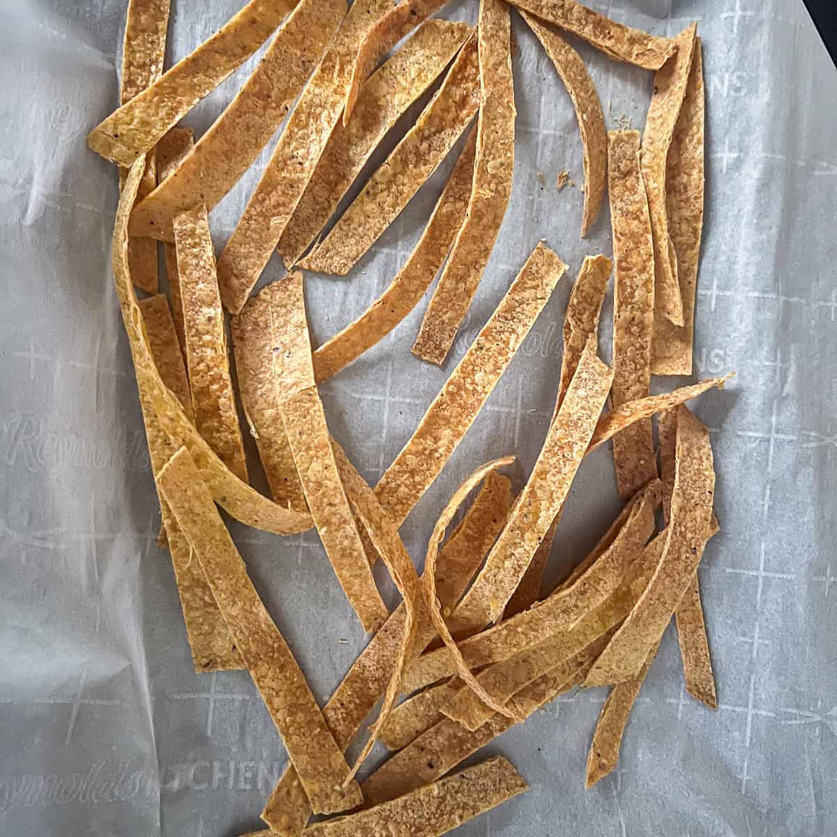 Baked cut tortilla strips on a parchment lined baking sheet.