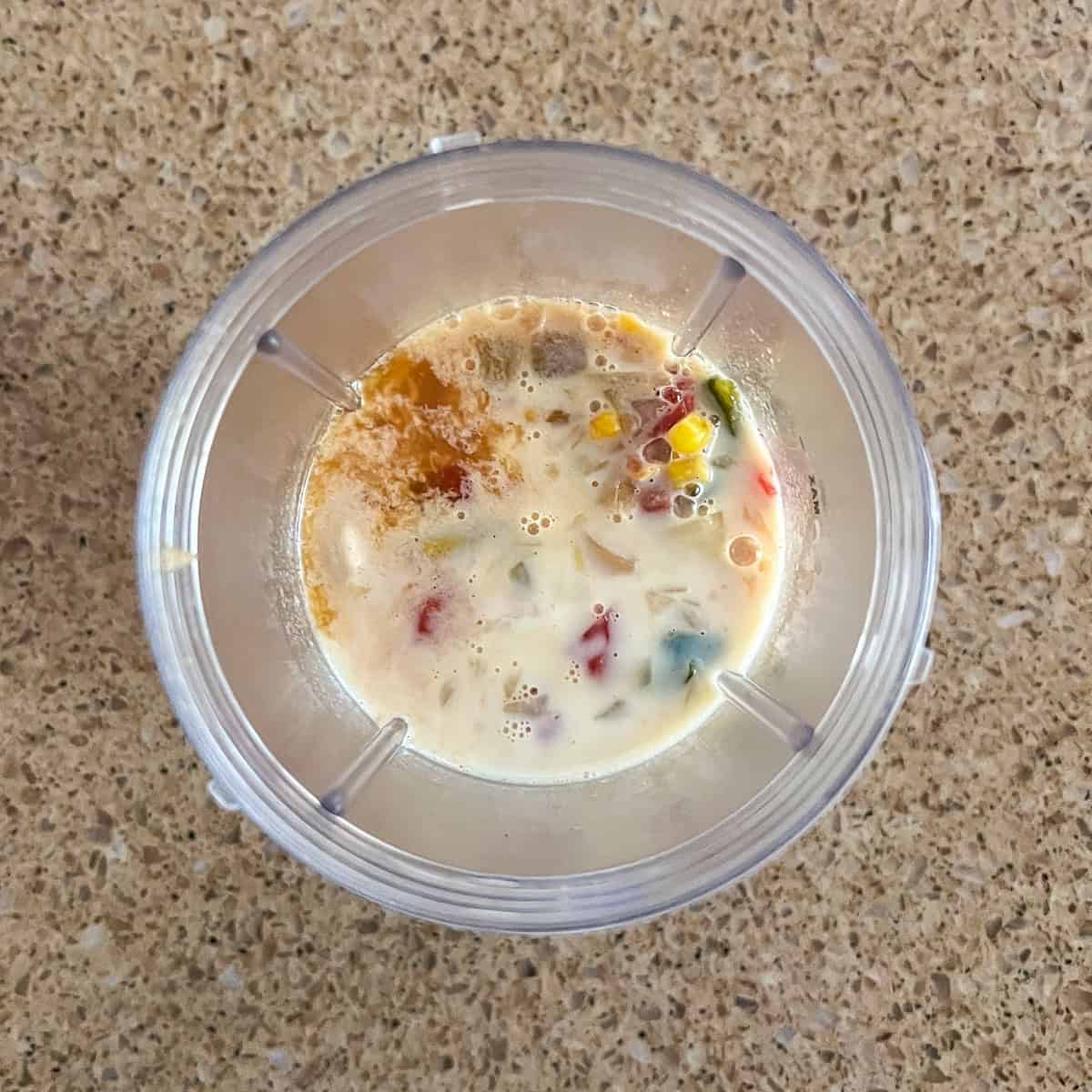 Some of the soup mixture with cashews and soy milk in a bullet blender cup.