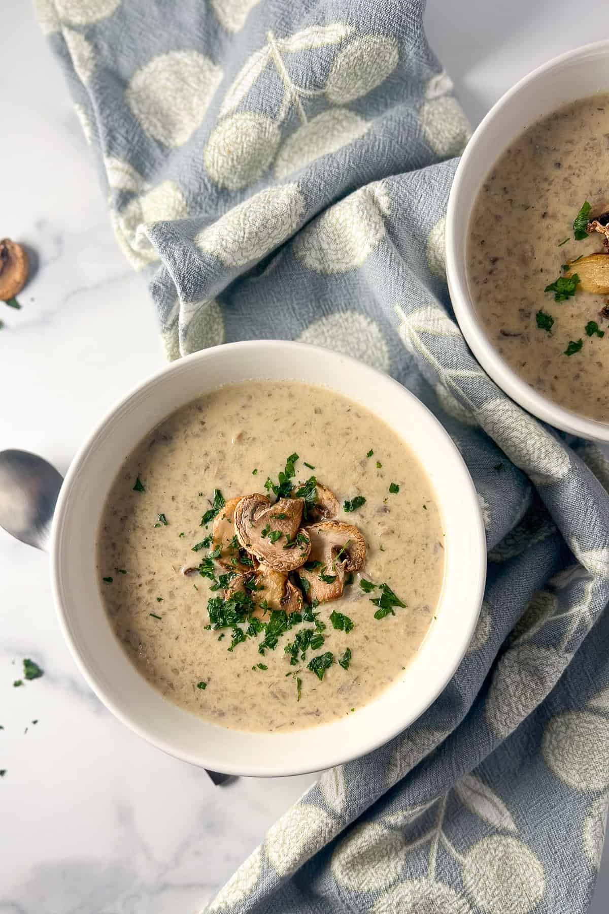 Vegan cream of mushroom soup in a bowl, topped with cooked mushrooms and chopped parsley.