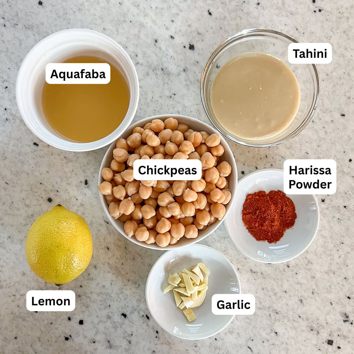Ingredients for harissa hummus: chickpeas, tahini, aquafaba, harissa powder, garlic, and lemon.
