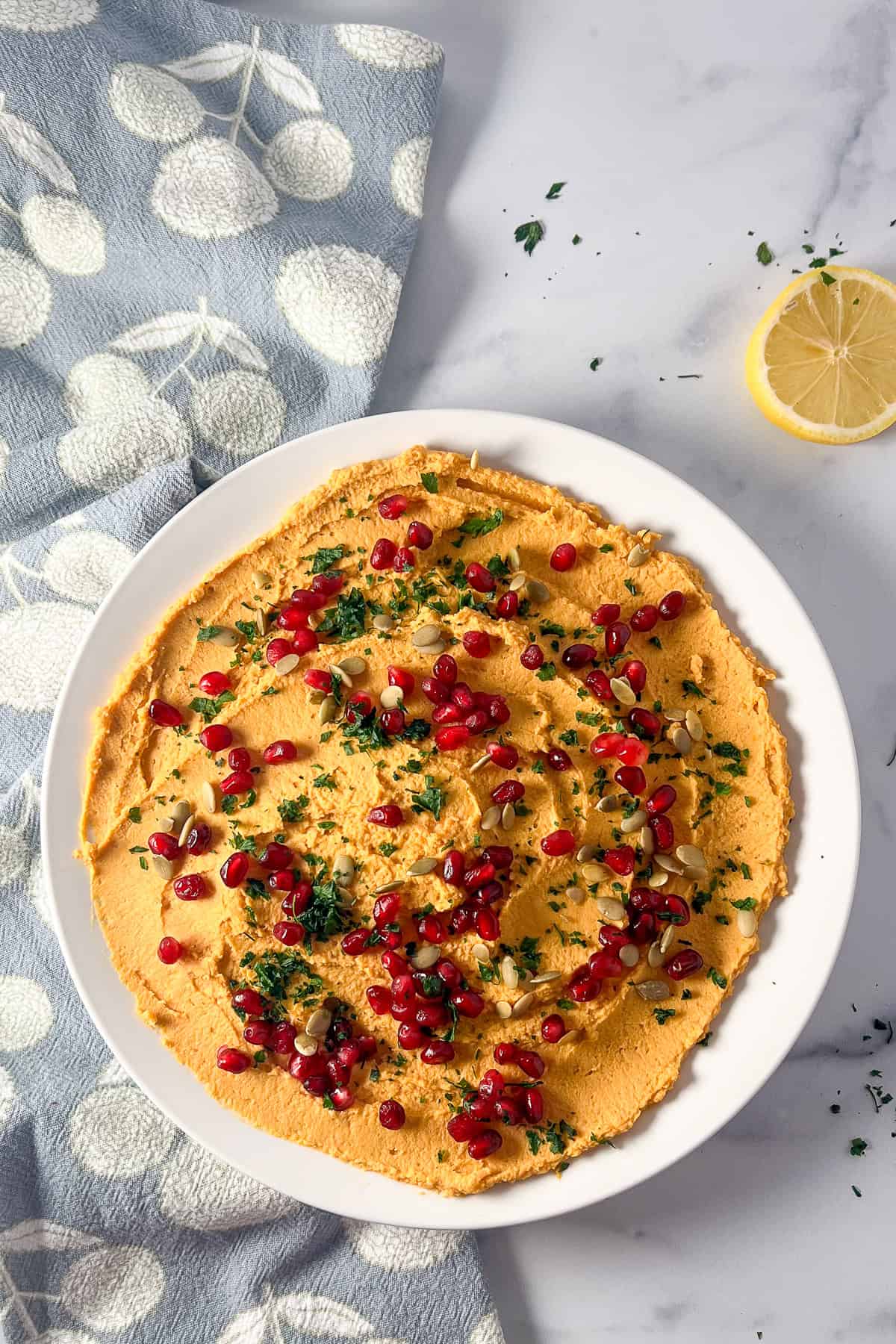 A bowl of hummus topped with pomegranate arils, pumpkin seeds and chopped parsley.