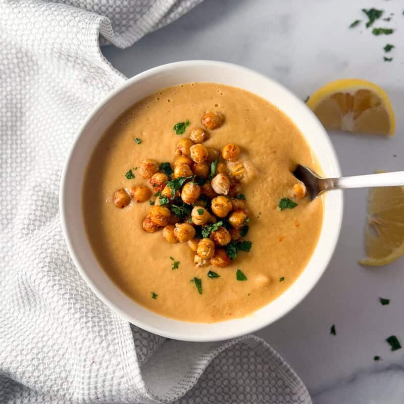 A bowl of roasted cauliflower soup topped with roasted chickpeas and fresh herbs.