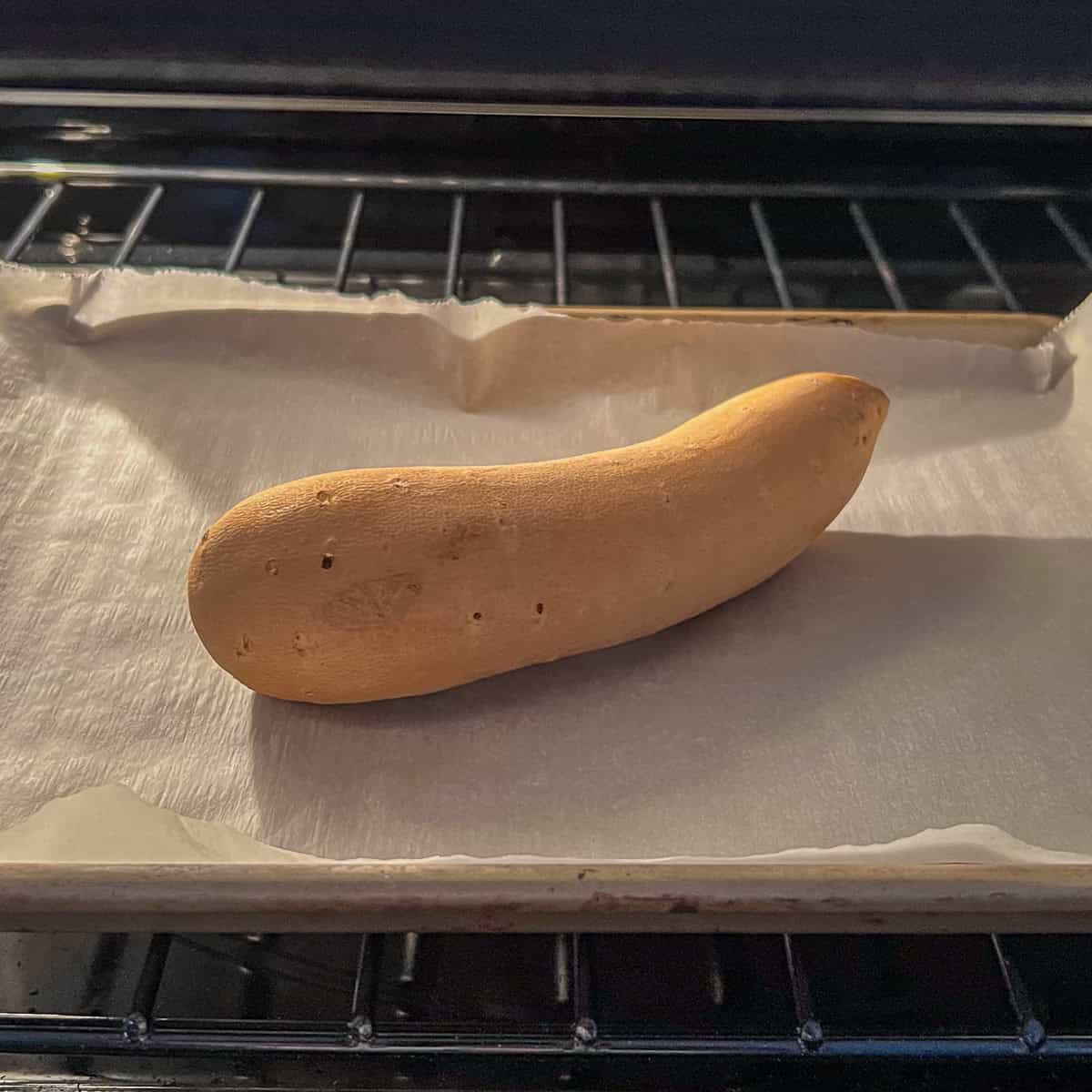 A small white sweet potato on a parchment lined baking sheet.