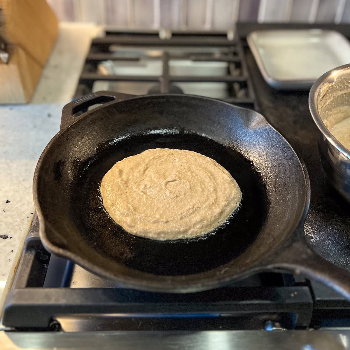 A vegan eggnog pancake being cooked in a cast-iron skillet on the stovetop.