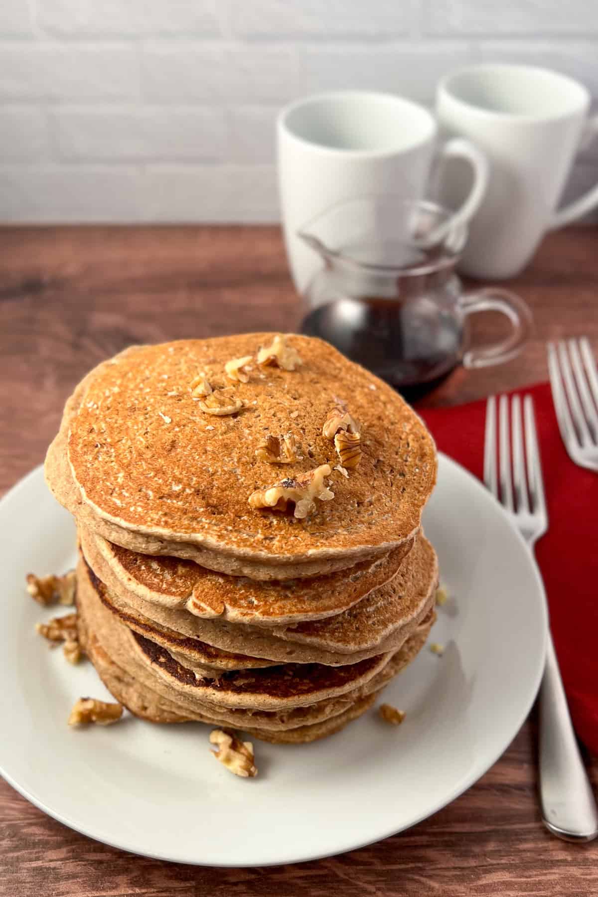 A big stack of vegan eggnog pancakes on a plate topped with chopped nuts.