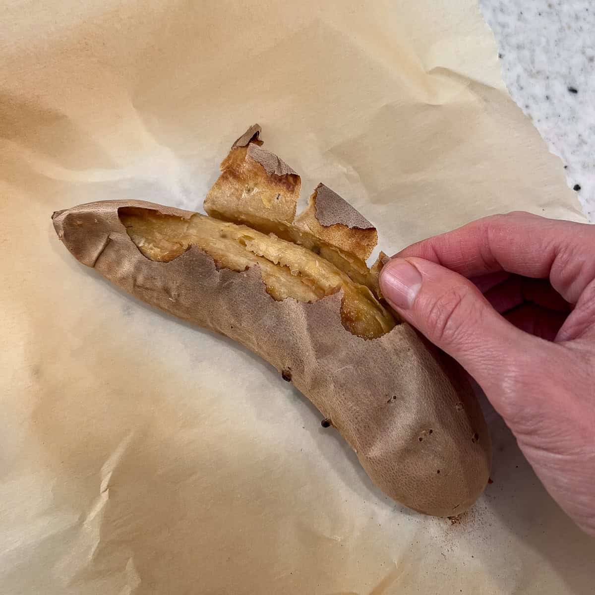 A woman's hand peeling the skin off the sweet potato after it's been baked and cooled.