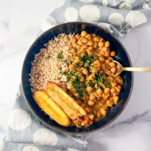 Jamaican Chickpea Curry in a bowl with brown rice and plantains on the side.