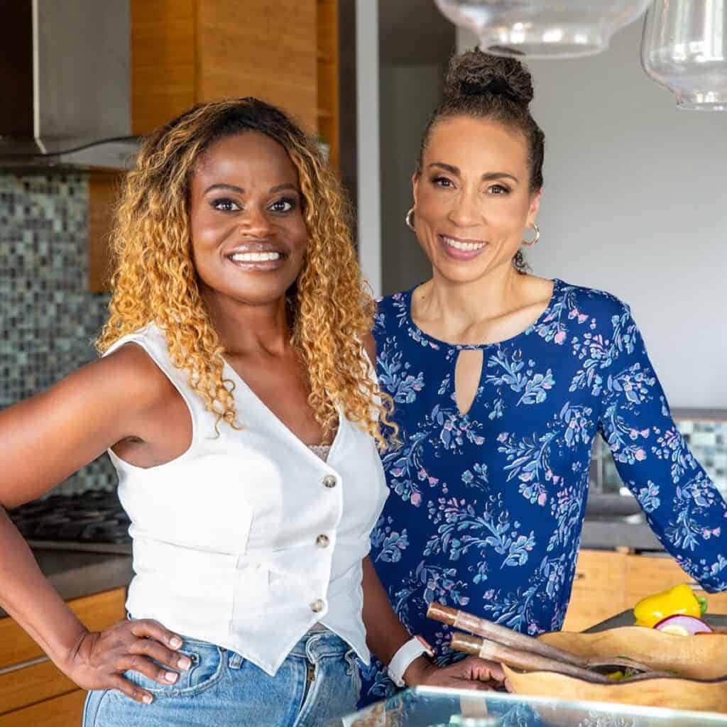 Two women in the kitchen smiling.