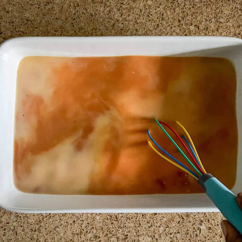 Coconut milk and broth being combined with a whisk in the casserole dish.