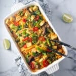 Baked Asian Noodles with veggies and tofu in a casserole dish, with lime wedges and tongs on the side.