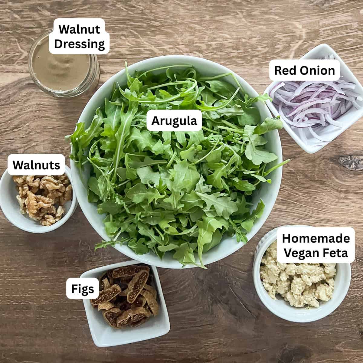 Ingredients for arugula fig walnut salad: arugula, walnut dressing, red onion, walnuts, dried figs, and homemade vegan feta.