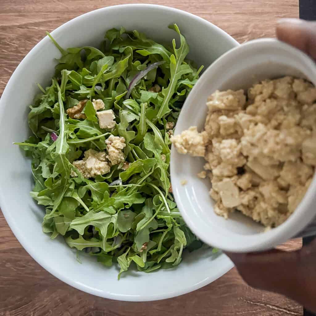 Homemade vegan feta being added to the arugula.