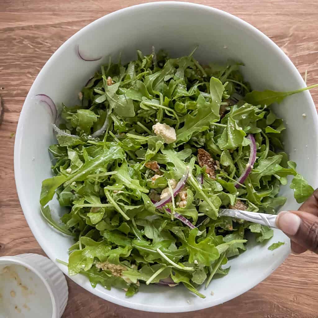 A woman's hand using a spoon to combine salad ingredients.