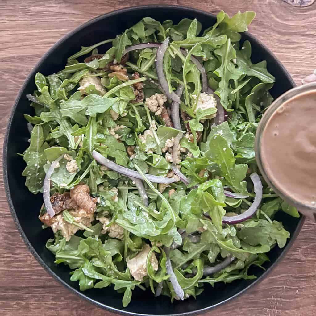 Walnut dressing being drizzled on top of the arugula fig and walnut salad.