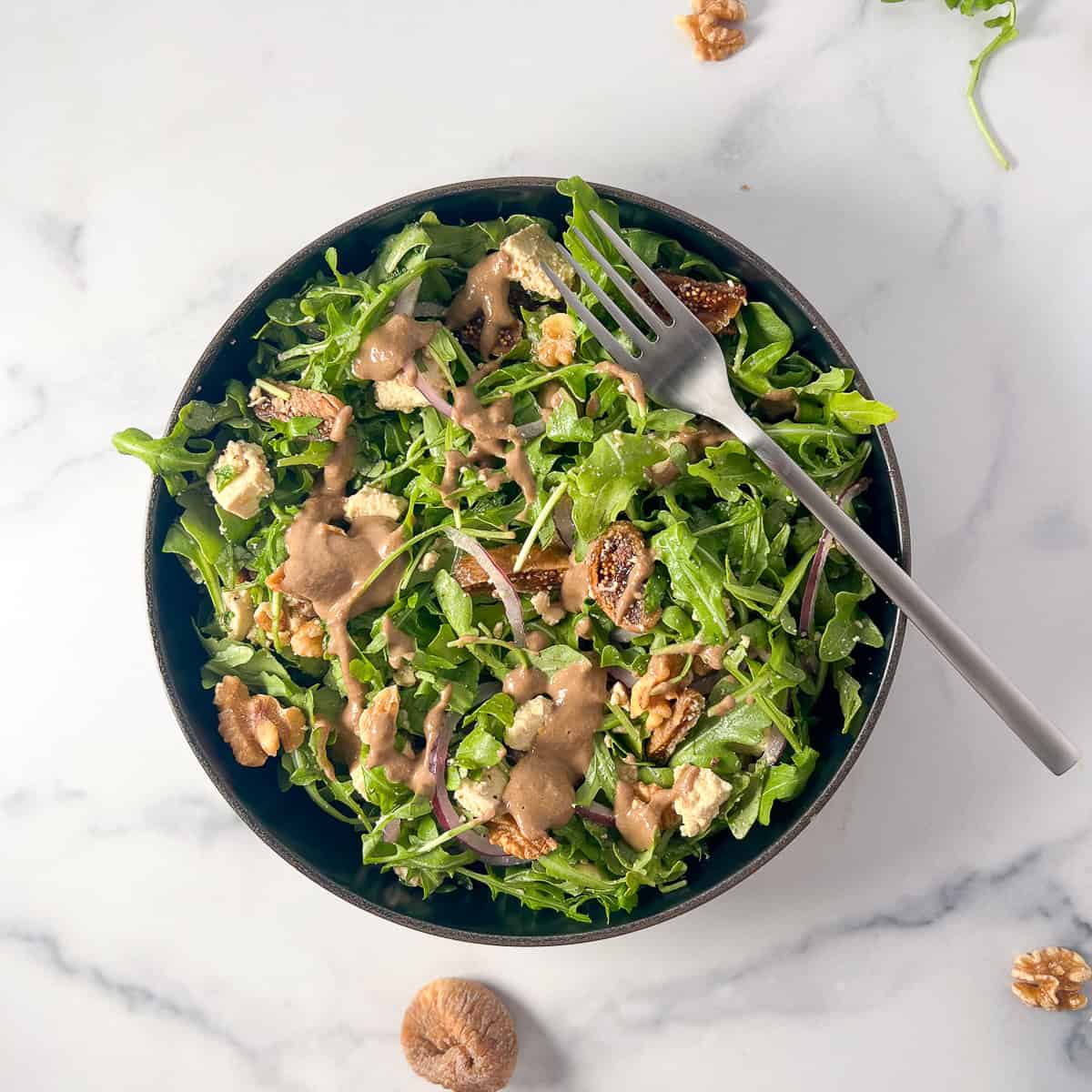 Arugula fig and walnut salad in a bowl with a fork balanced on the side of the bowl.