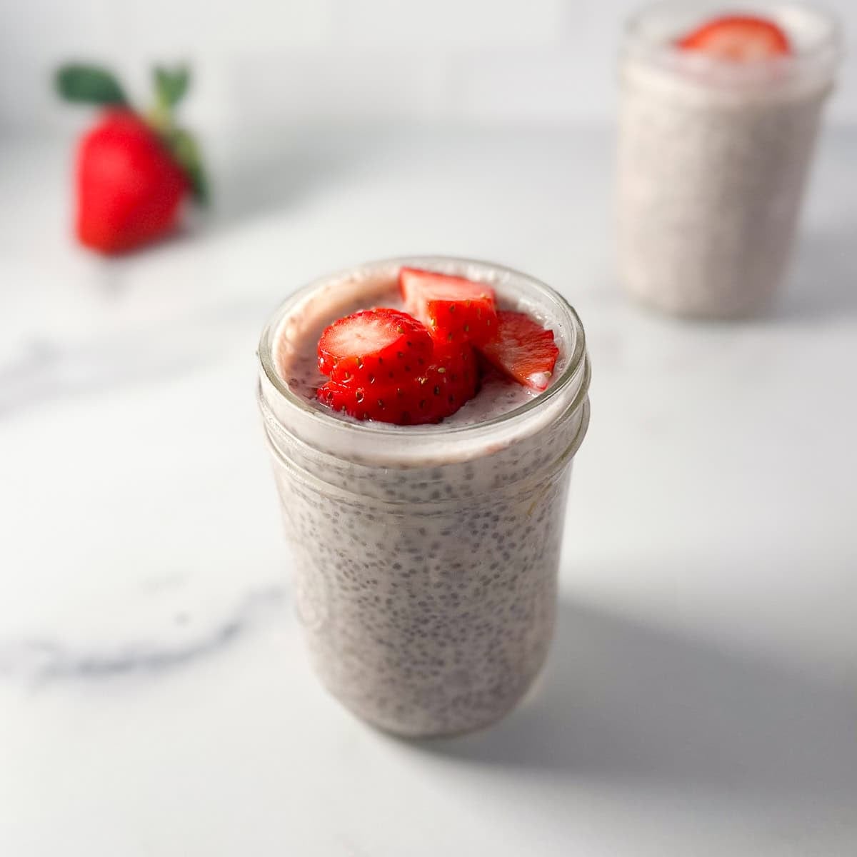A mason jar with chia strawberry pudding topped with fresh chopped strawberries.