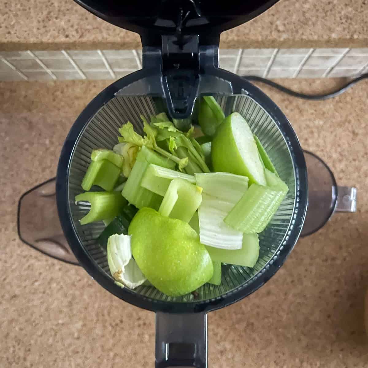 Celery, cucumbers, green apples and lemons in a juicer shuttle before juicing.