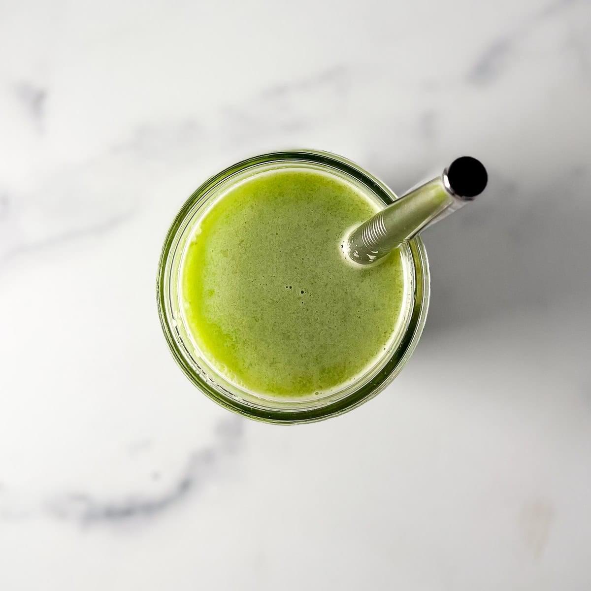 Celery cucumber juice in a glass with metal straw.