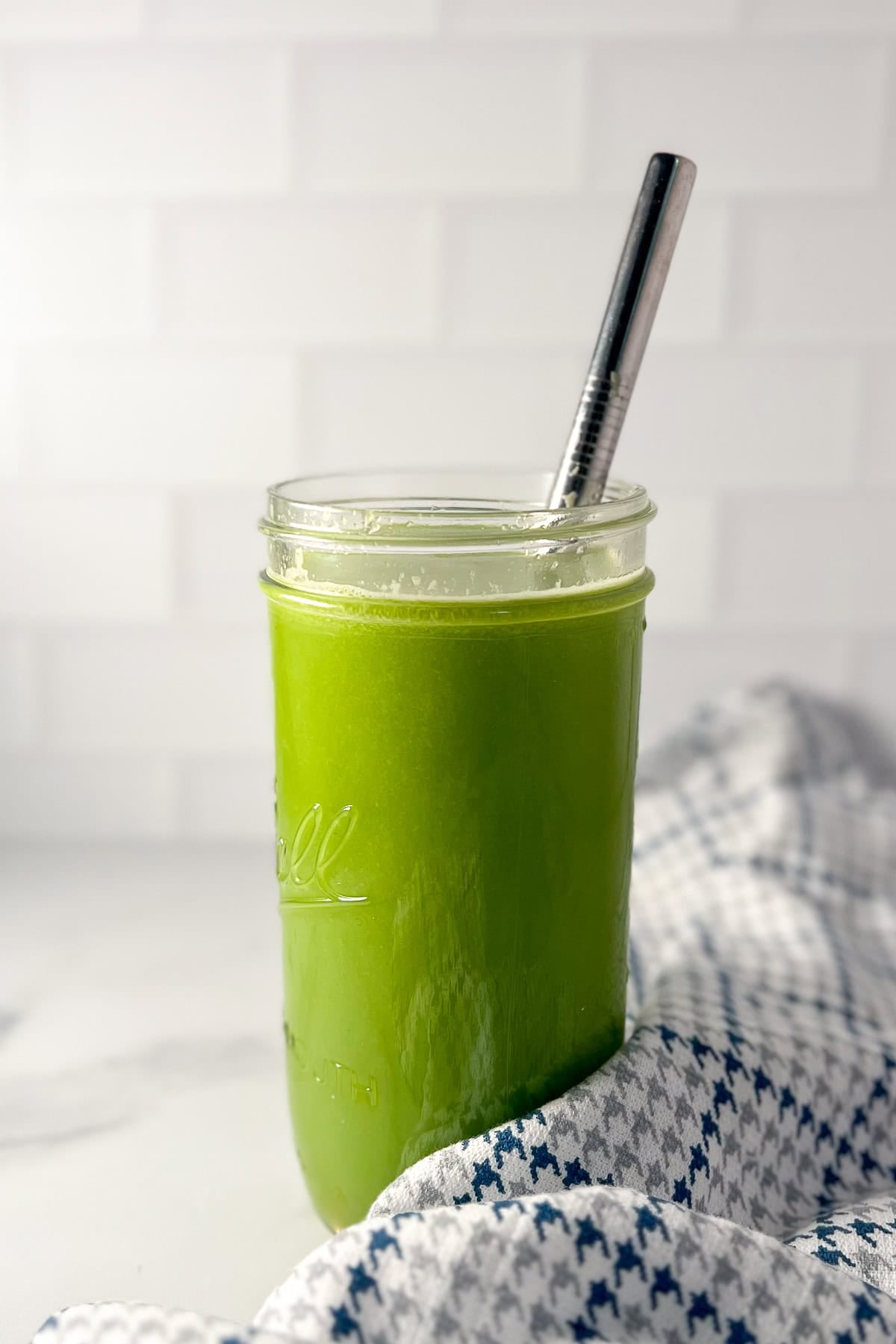 Celery cucumber apple and lemon juice in a tall glass with a straw, napkin on the side.
