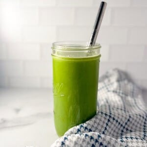 Celery cucumber juice in a tall glass with a metal straw.