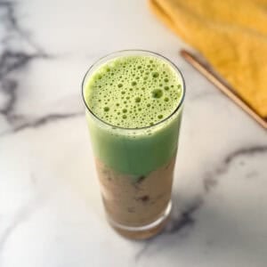 Iced peach matcha latte in a tall glass with a straw on the side.