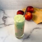 Iced peach match latte in a tall glass with straw and fresh peaches in the background.