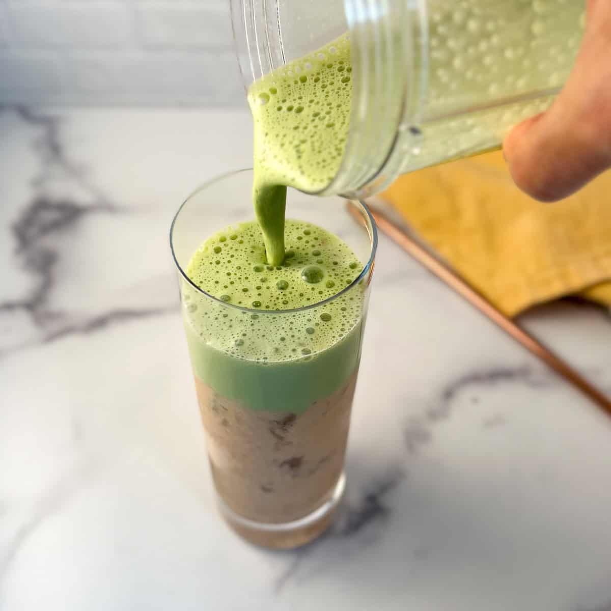 Matcha mixture being added to the peach milk mixture in a tall glass with ice.