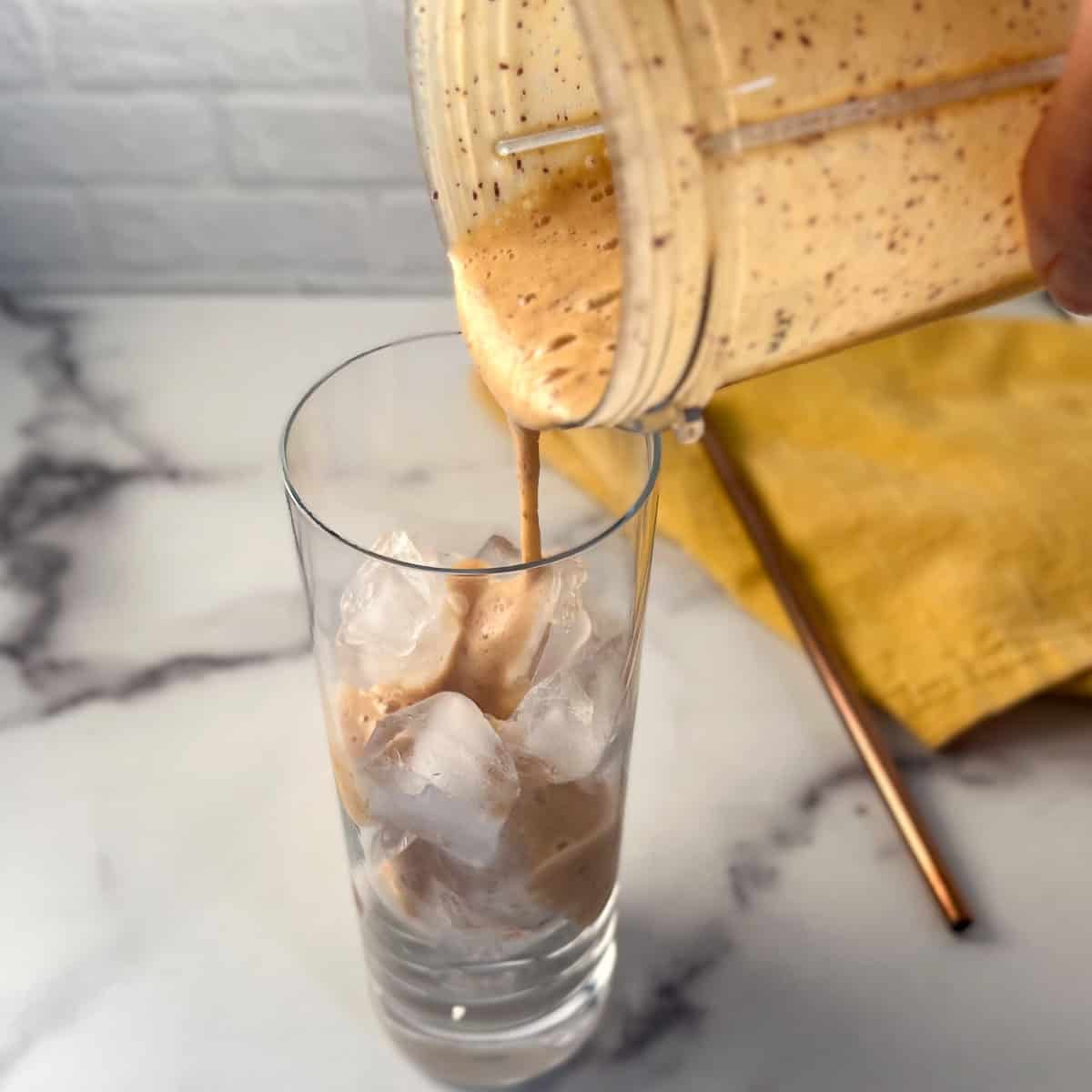 Peach milk mixture being added to a tall glass with ice.