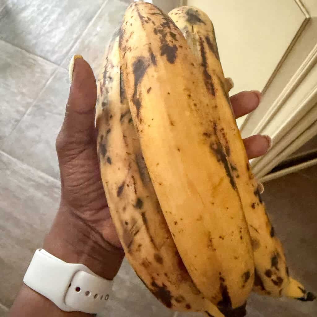 Woman holding ripe plantains in her hand. They are yellow with black spots.