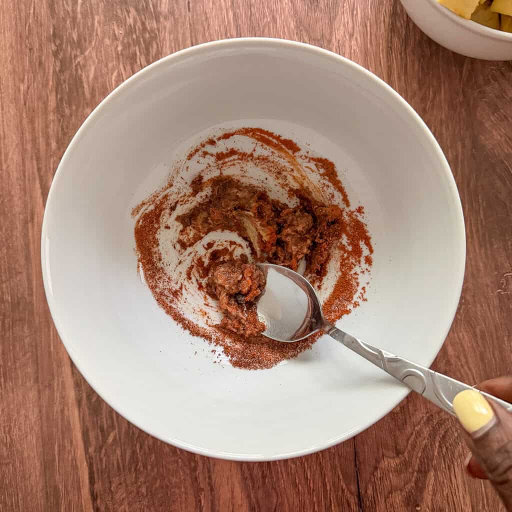 Garlic paste, ginger paste and dried seasonings being mixed in a bowl with a spoon.