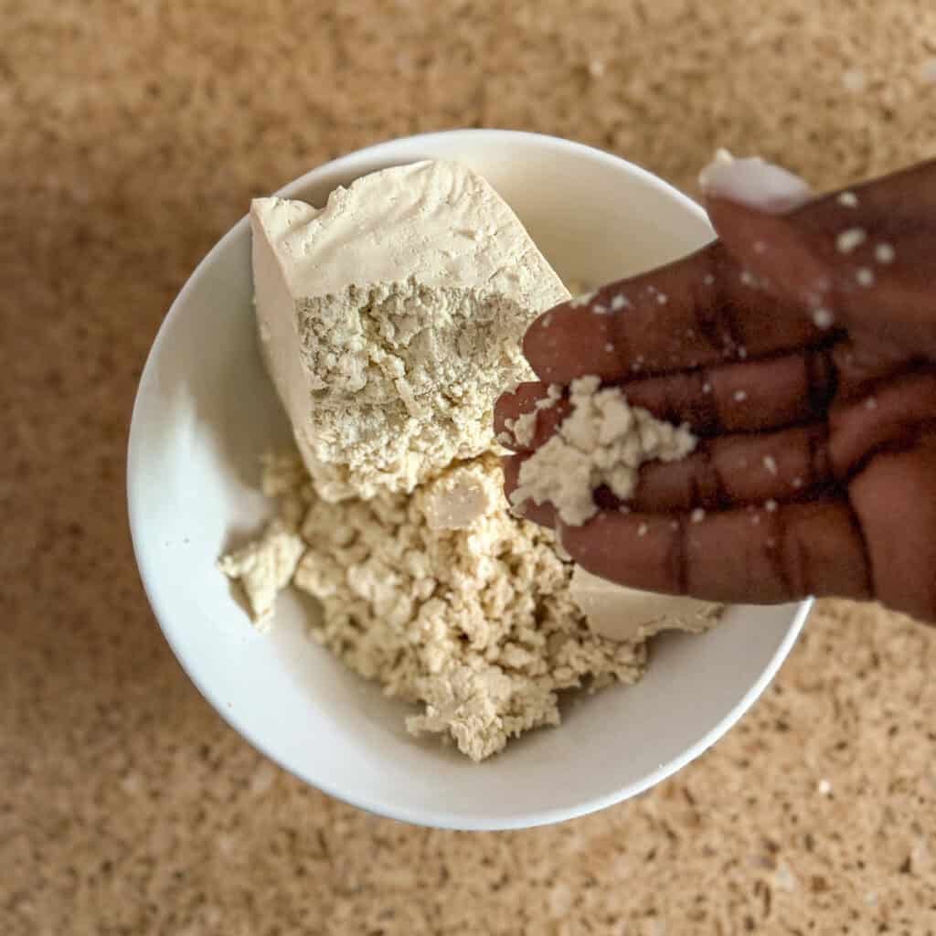 A woman's hand crumbling firm tofu.