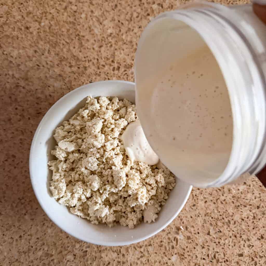 The blended silken tofu mixture being poured into the crumbled firm tofu.