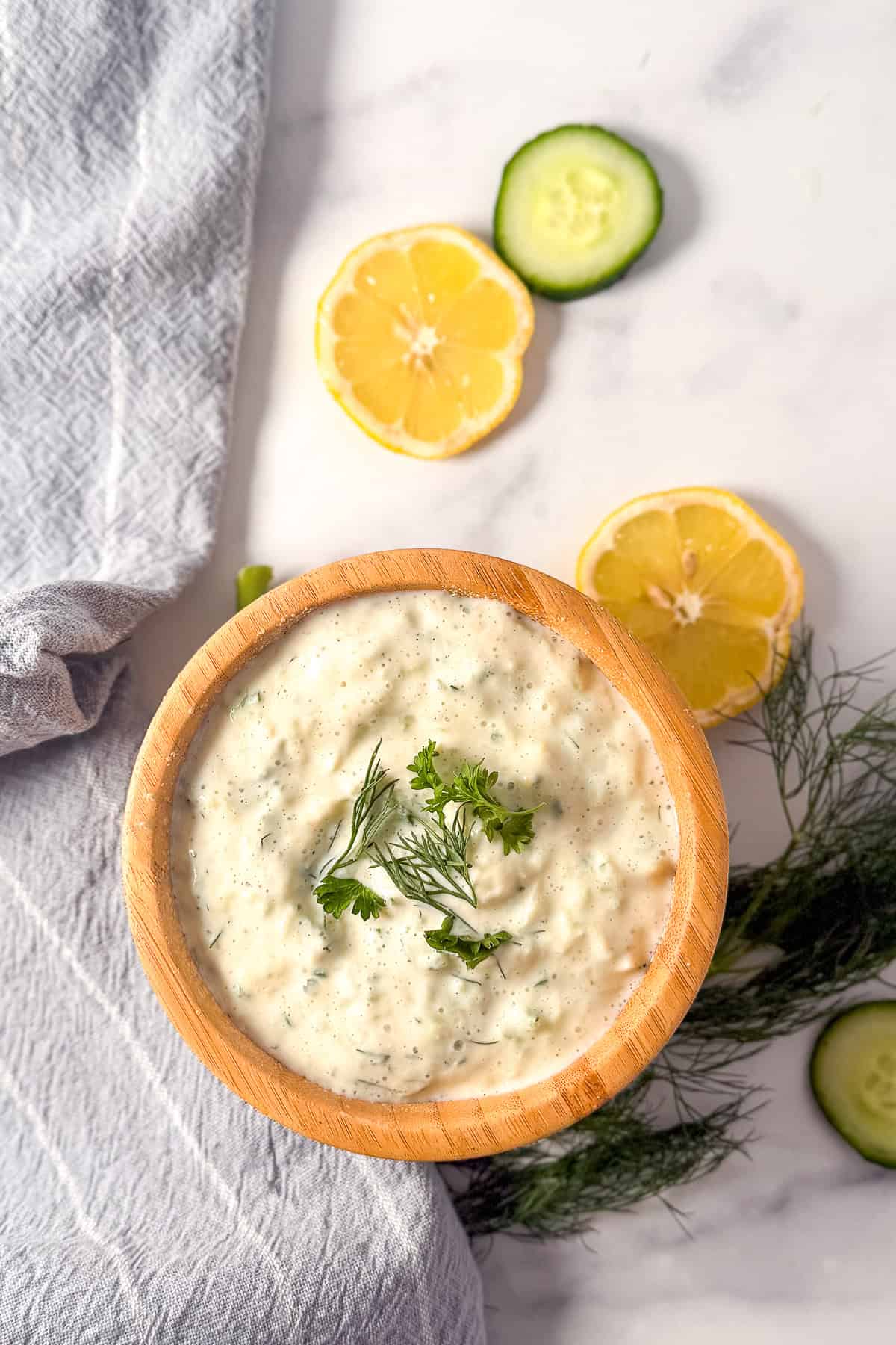 Vegan tzatziki in a wooden bowl with sliced lemon and cucumber in the background.