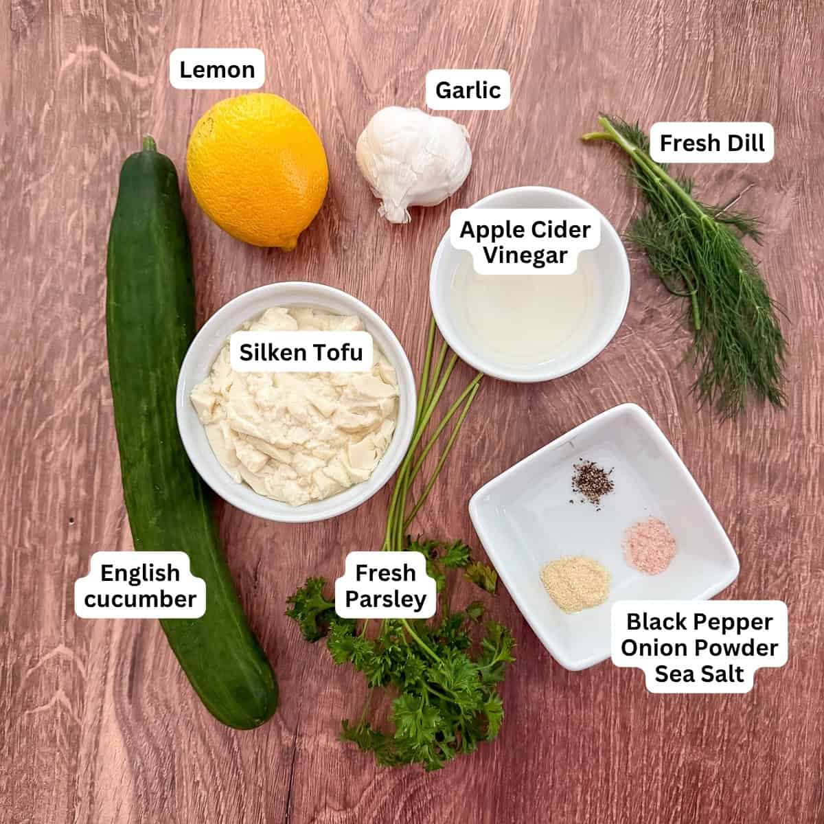 Ingredients for homemade vegan tzatziki sauce: silken tofu, english cucumber, lemon, garlic, apple cider vinegar, fresh dill, fresh parsley, and seasonings.