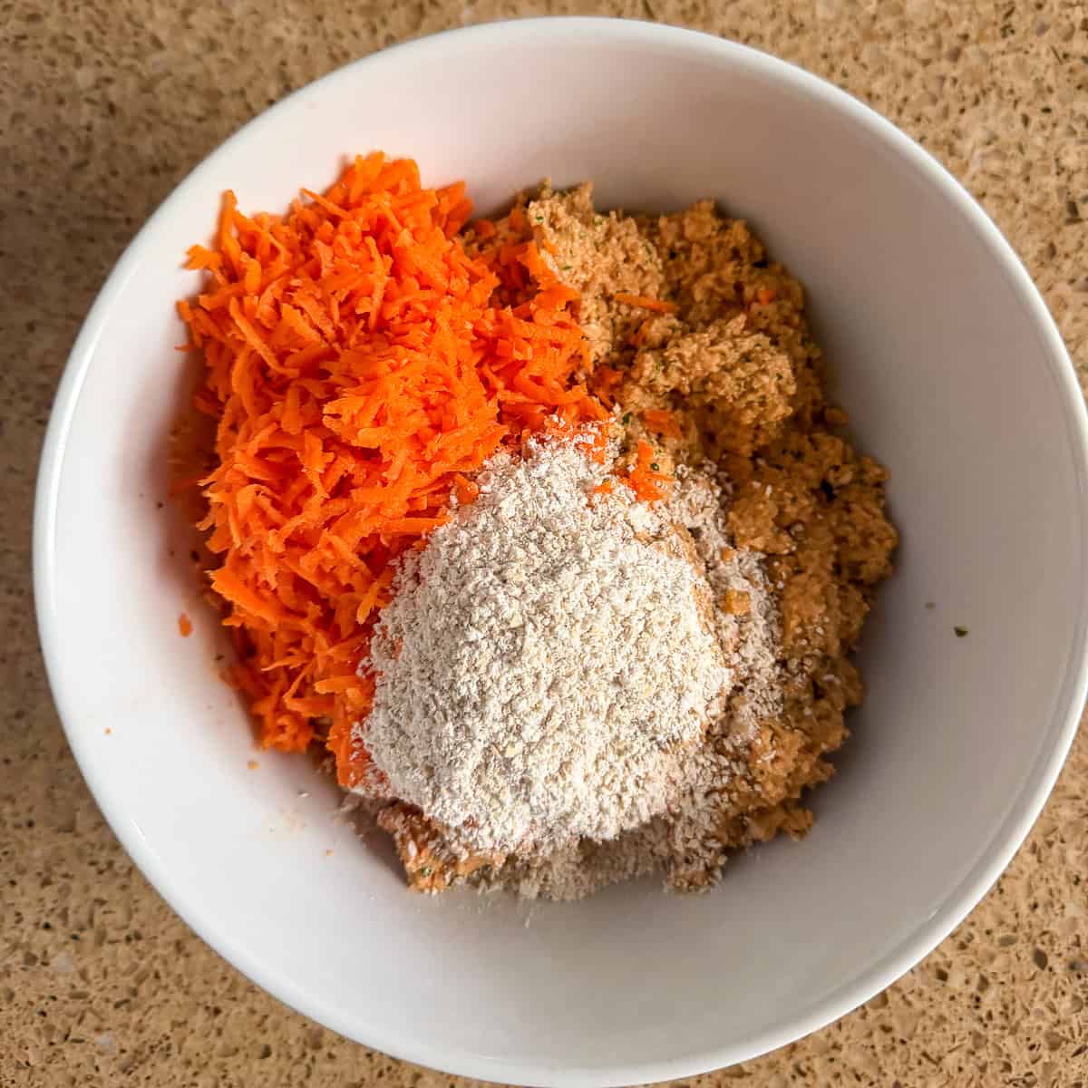 Lentil mixture in a mixing bowl with finely grated carrot and oat flour.