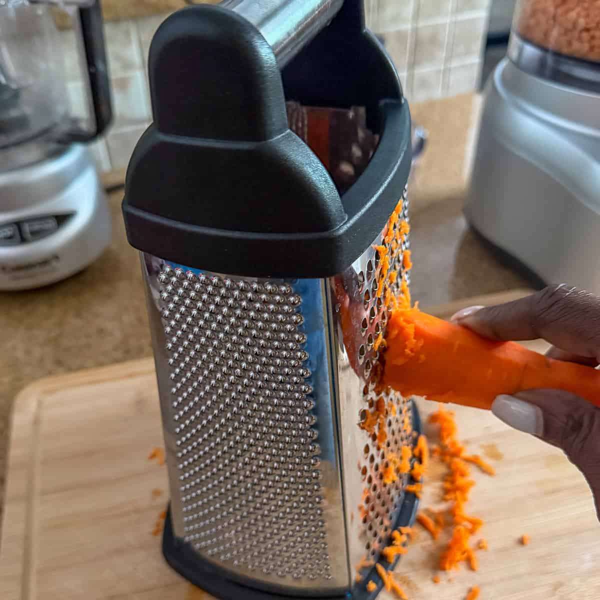 A woman's hand grating a carrot with a box grater.