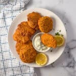 A plate of red lentil fritters with sauce and lemon slices on the side.