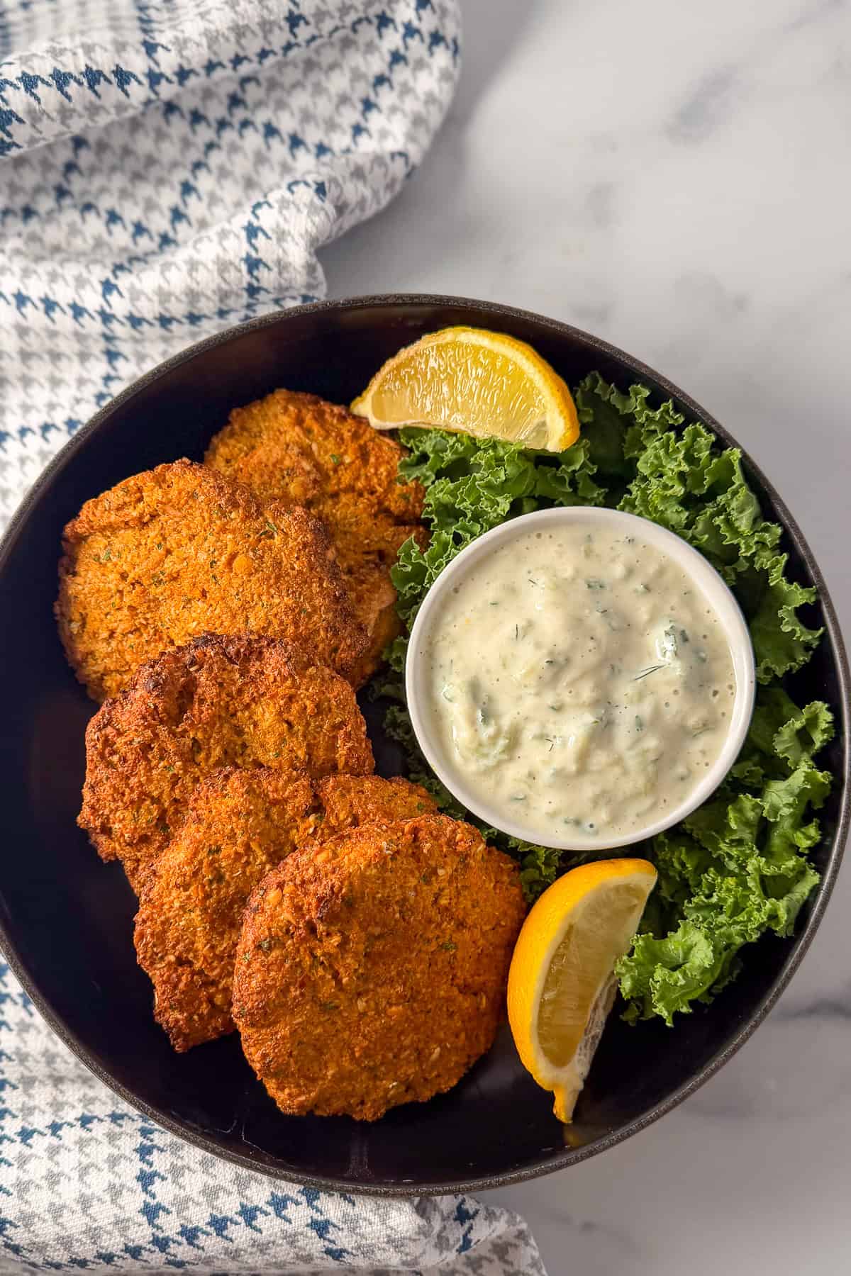 A plate of red lentil fritters with fresh lemon and vegan tzatziki sauce on the side.