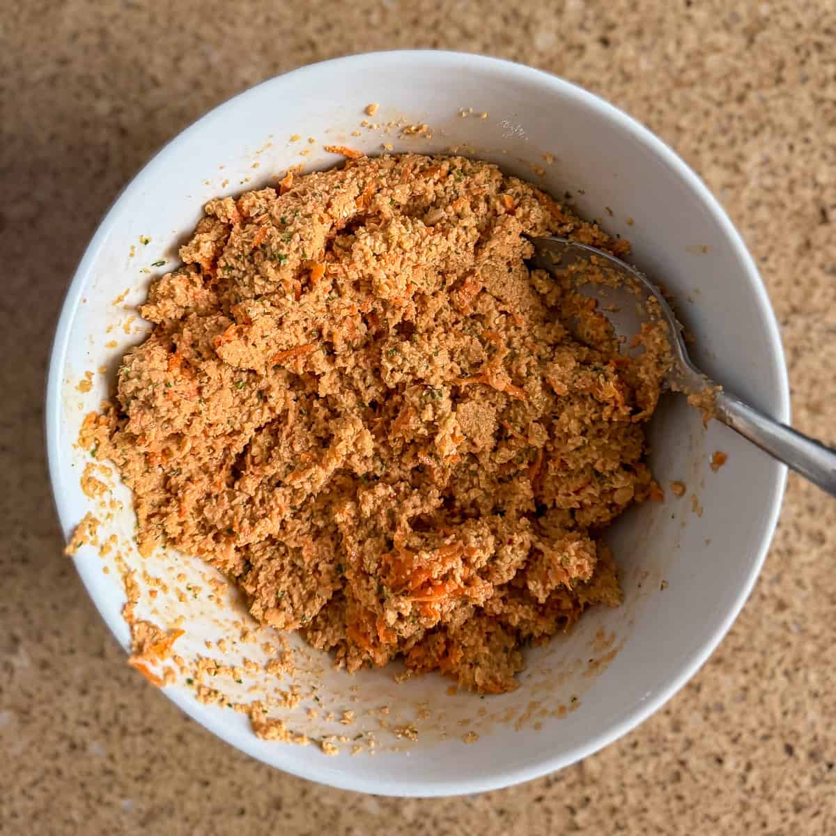Red lentil mixture combined in a bowl with grated carrot and oat flour.