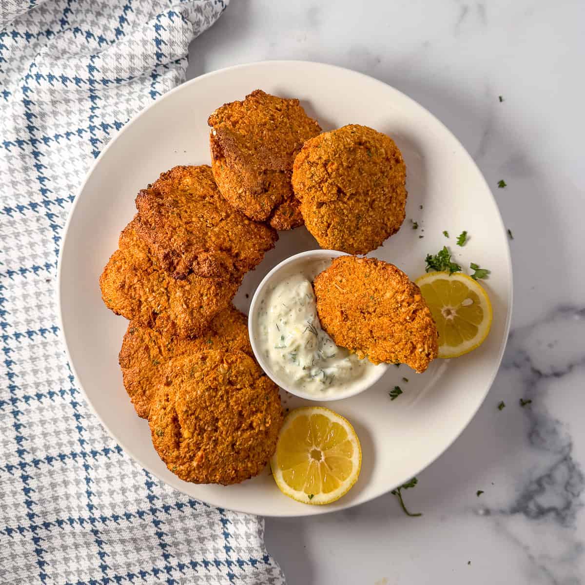 A plate of red lentil fritters with sauce and lemon slices on the side.