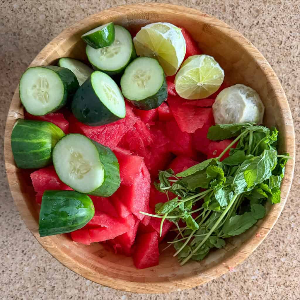Chopped watermelon, cucumber, limes and mint in a bowl.